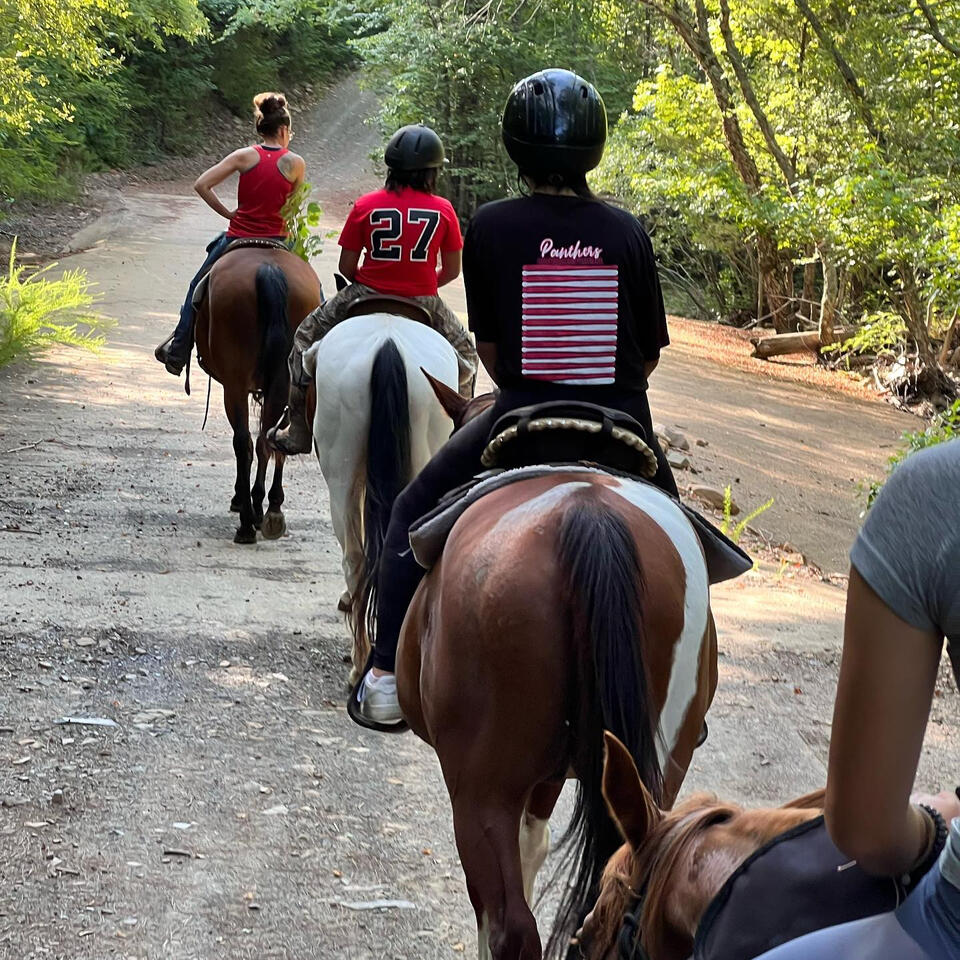 three people horse back riding down a trail